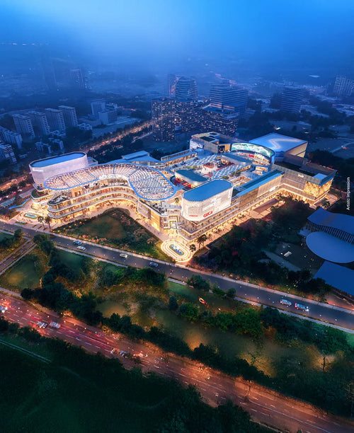 Aerial night view of Joy District AIPL, a modern retail and entertainment complex in a bustling urban area, showcasing illuminated architecture and vibrant storefronts.